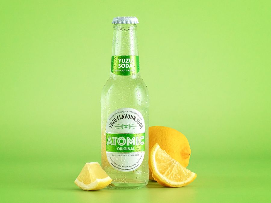 Atomic Yuzu Soda bottle with fresh lemons on a green background